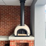 Brick oven elegantly placed on a brick wall, emphasizing its classic design and functional outdoor cooking space.