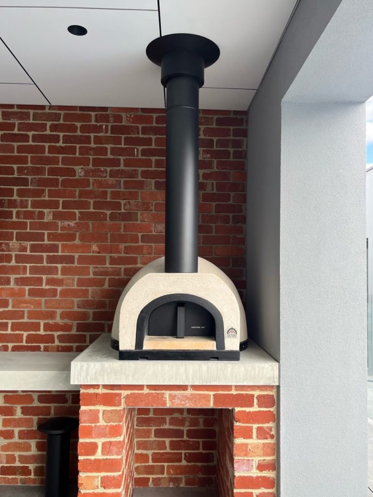 Brick oven elegantly placed on a brick wall, emphasizing its classic design and functional outdoor cooking space.