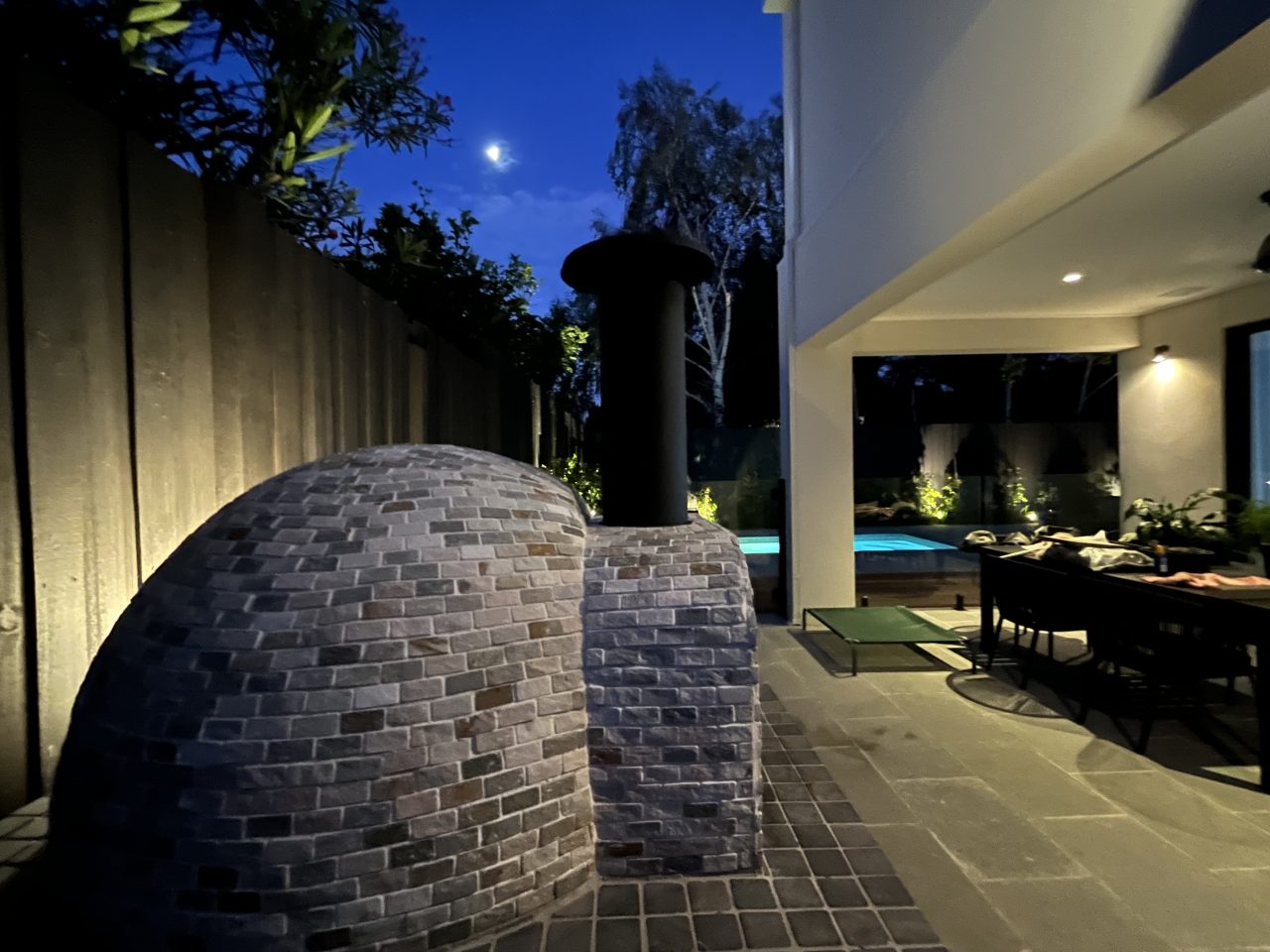 Stone pizza oven illuminated at night, set in a cozy backyard, creating a warm and inviting atmosphere.
