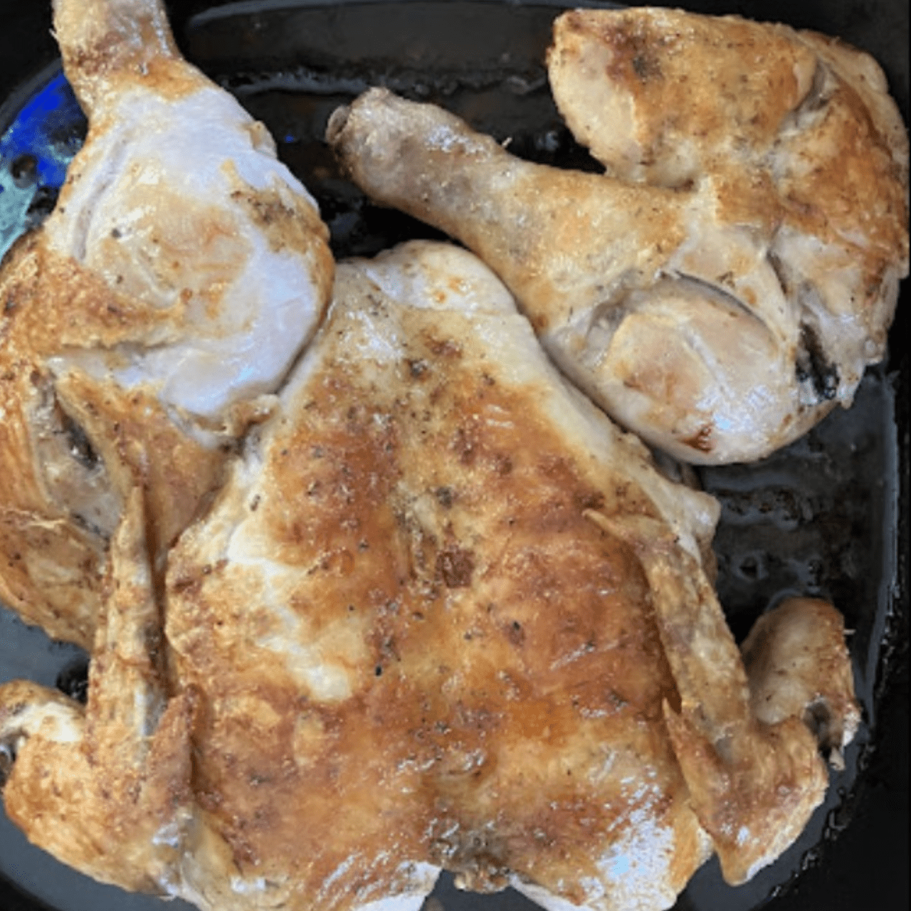 Whole chicken is placed on a black plate, highlighting its crispy texture and rich color.
